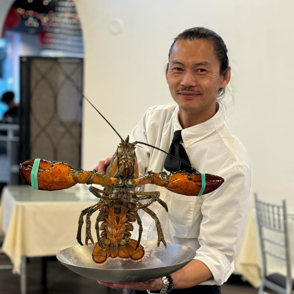 A Diamond Palace staff member holding a large live lobster on a metal platter, smiling at the camera.