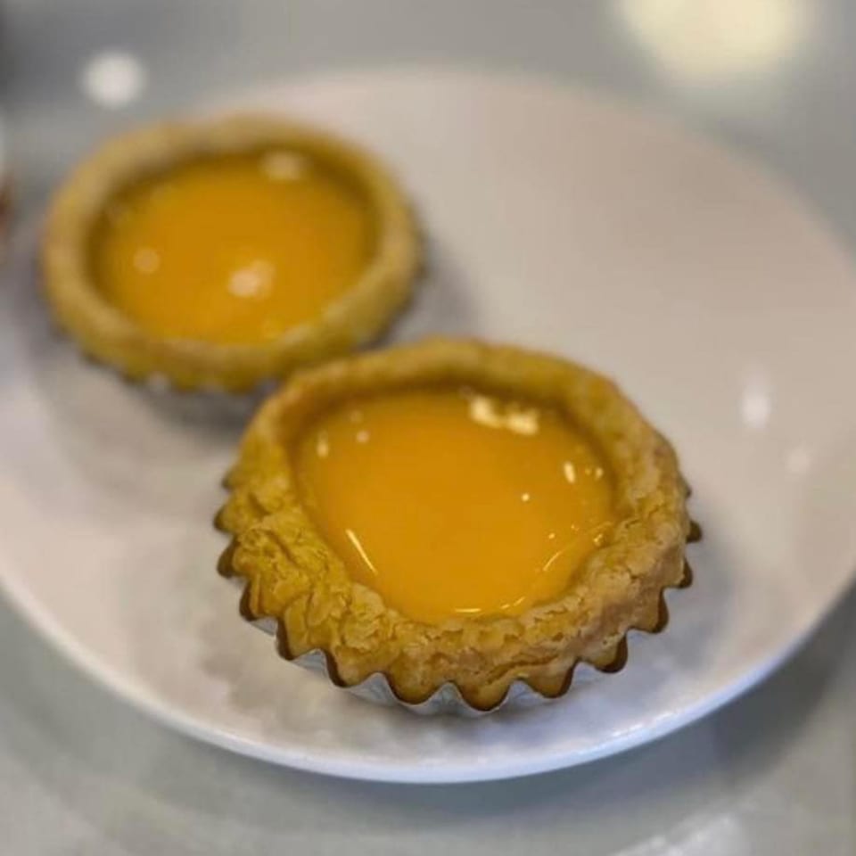Two golden Chinese egg tarts with bright yellow custard filling on a white plate.