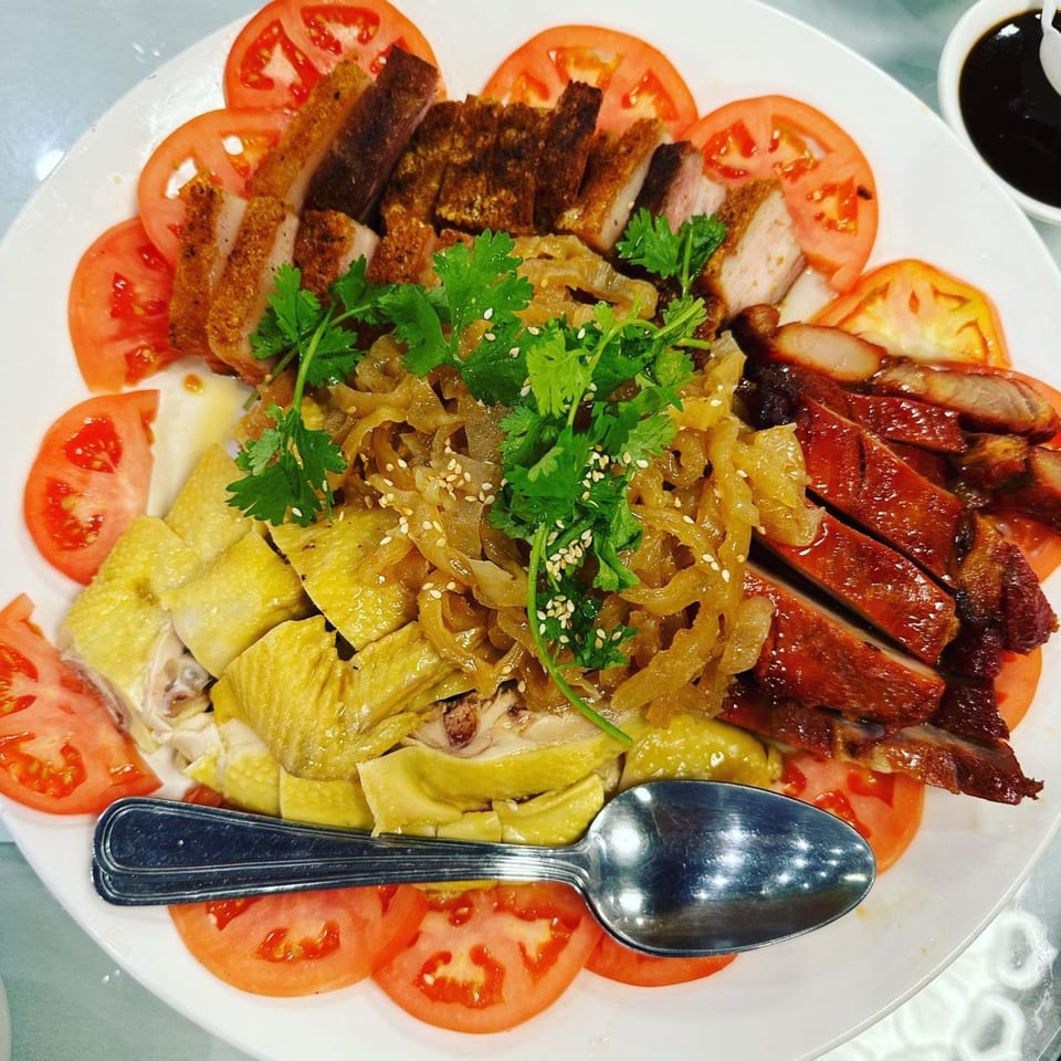 A large platter of sliced roasted pork, char siu, and poached chicken with jellyfish and tomatoes.