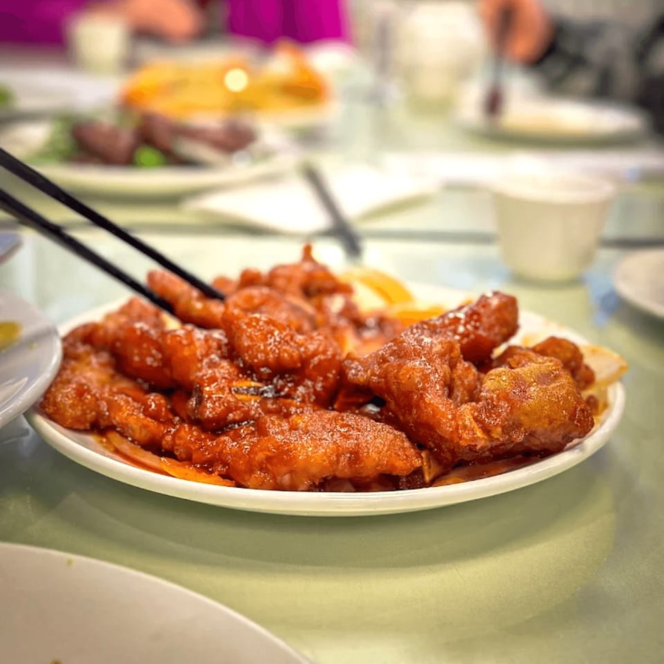 Chopsticks picking up a piece of sweet and sour pork from a white plate at Diamond Palace.