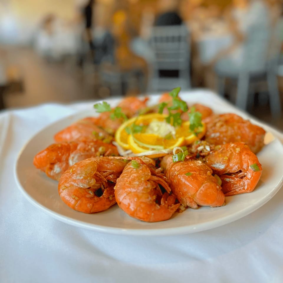 A white plate of cooked orange shrimp garnished with orange slices and green herbs.