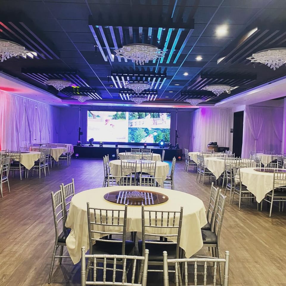 An empty Diamond Palace dining hall with round tables, silver chairs, and a large screen displaying images.