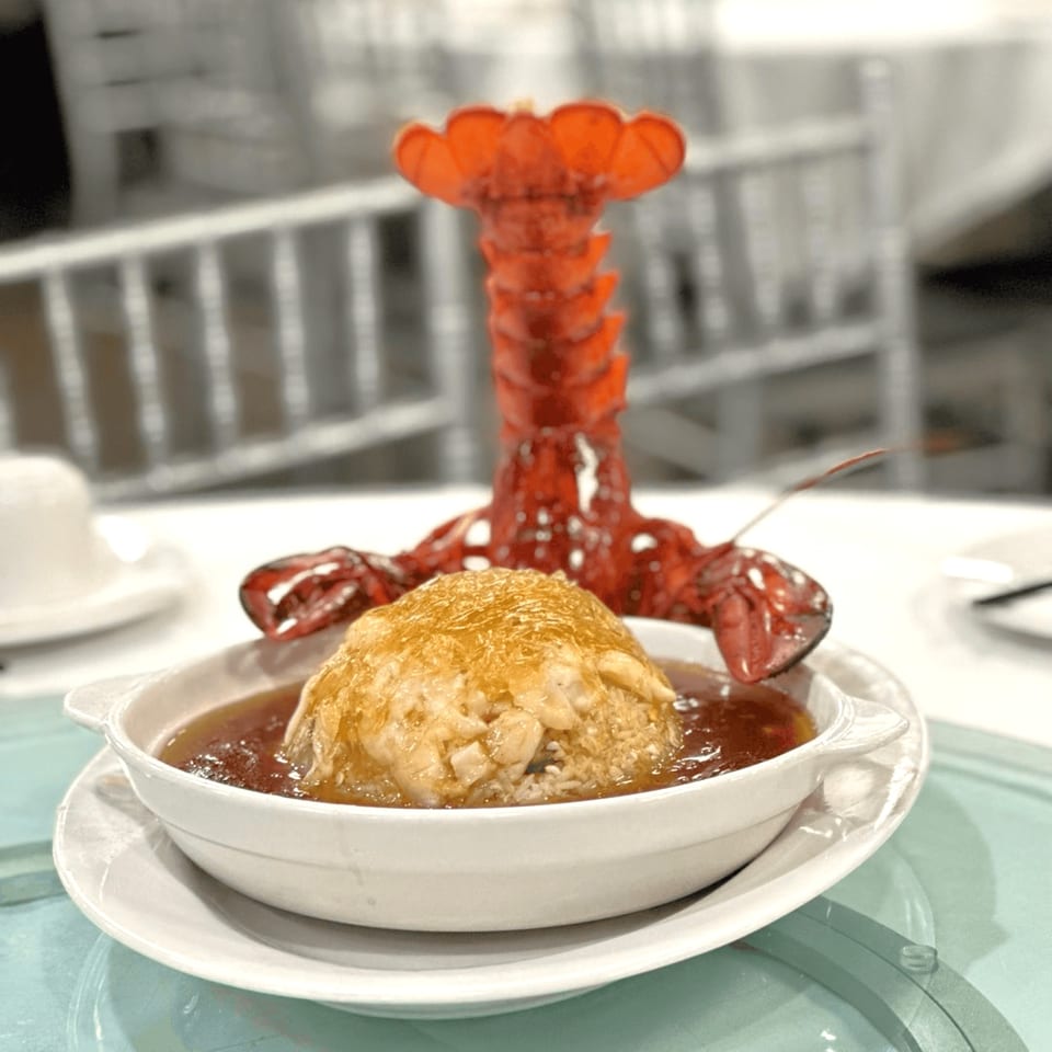 A Chinese dish with a mound of rice and seafood in sauce, garnished with a bright red lobster tail.