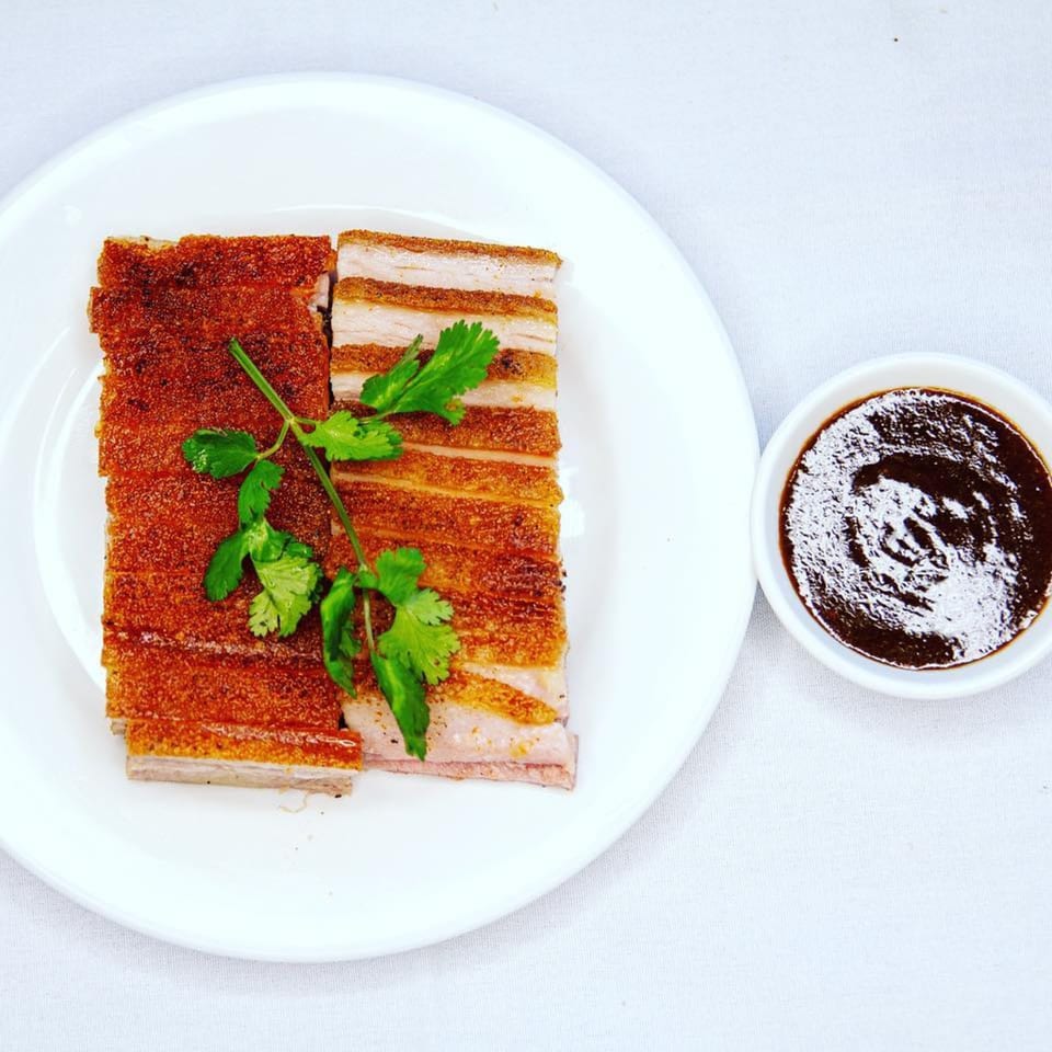 Crispy Chinese roasted pork belly slices with cilantro garnish and a side of dark dipping sauce.