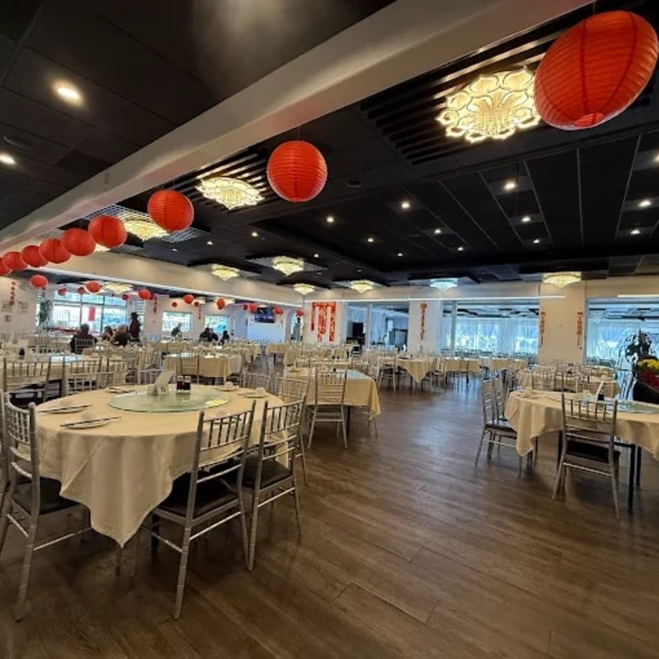 Spacious Diamond Palace dining room with round tables, white tablecloths, silver chairs, and red lanterns.