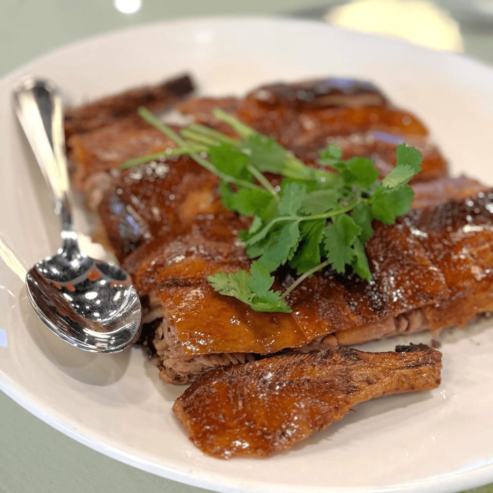 Platter of glistening roasted duck, garnished with fresh cilantro, and a spoon on a white plate.