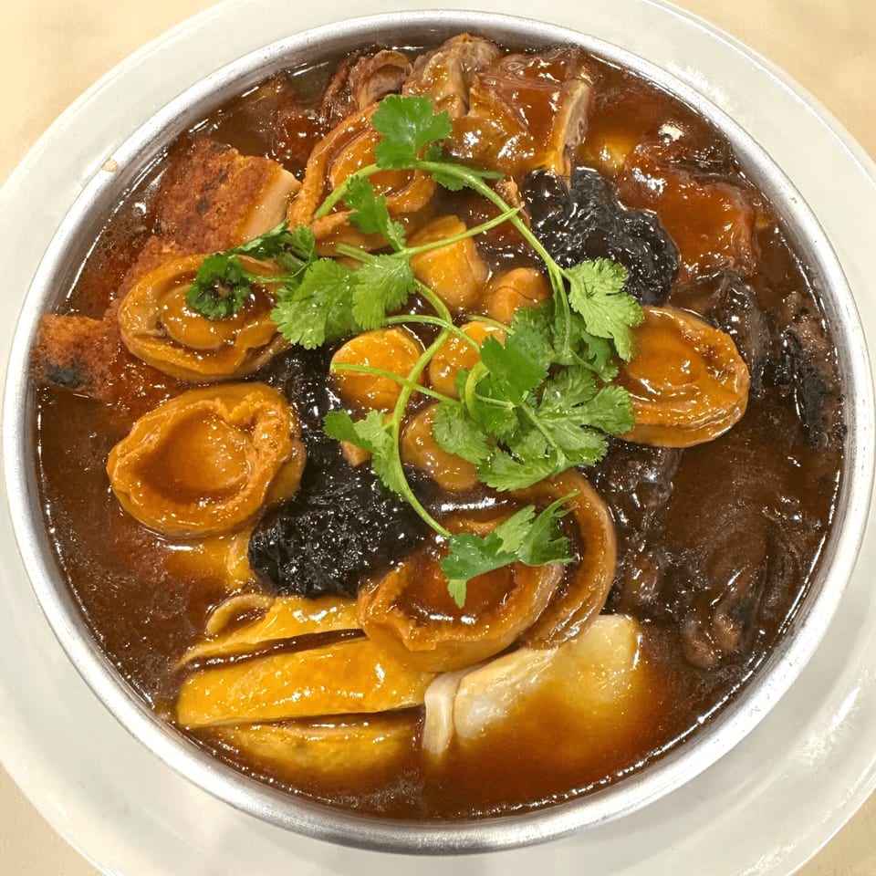 A close-up of a Chinese braised dish with abalone, mushrooms, and other ingredients in a rich brown sauce.