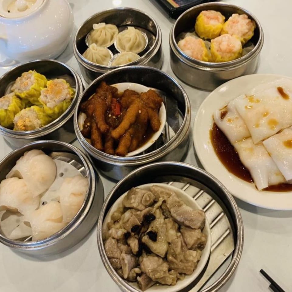 A variety of Chinese dim sum dishes, including dumplings, chicken feet, and rice rolls, on a white table.