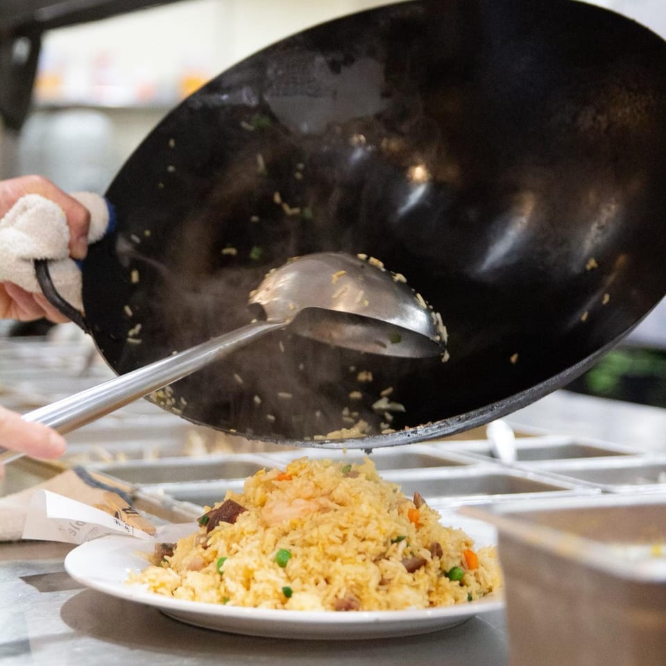 A chef serves steaming fried rice from a wok onto a white plate at Diamond Palace.