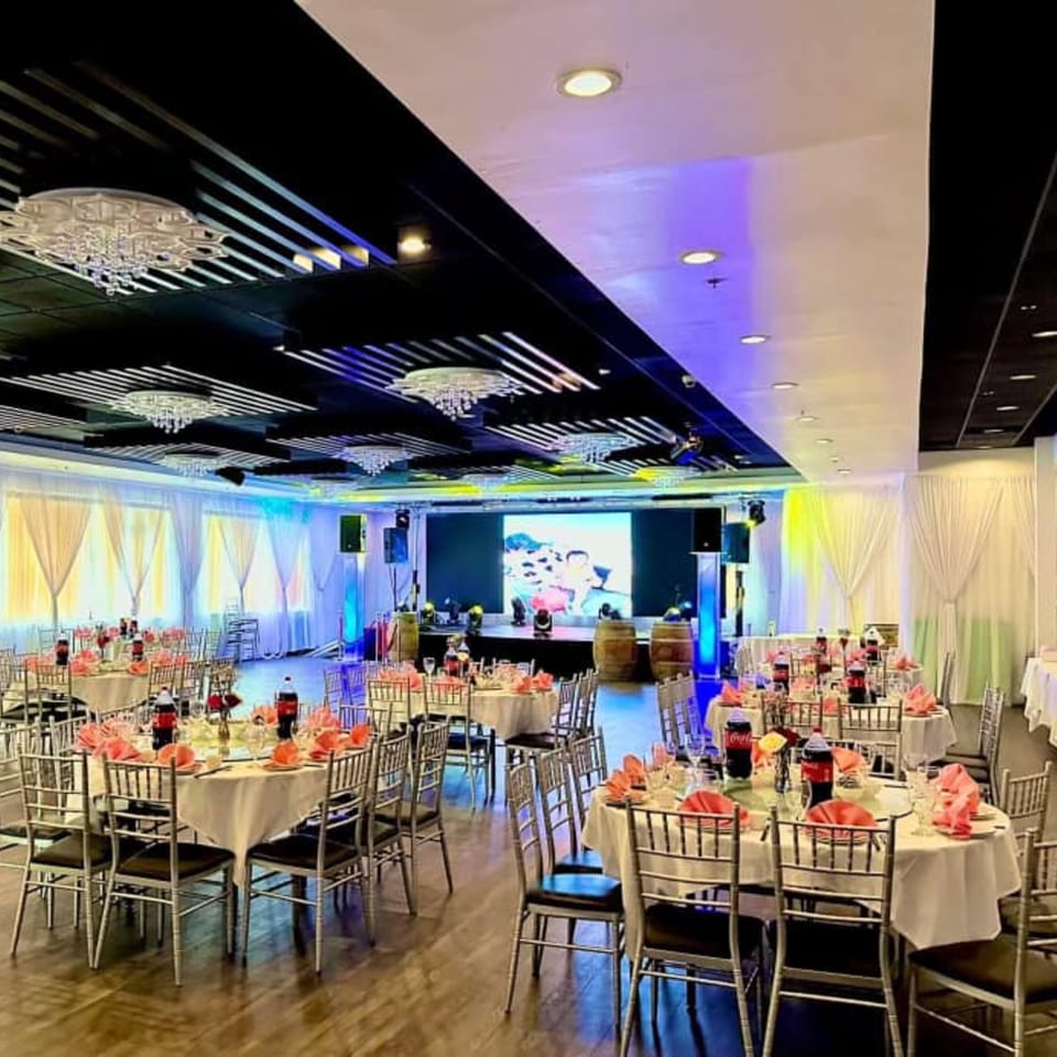 A large, empty banquet hall at Diamond Palace with round tables set with pink napkins and a stage.